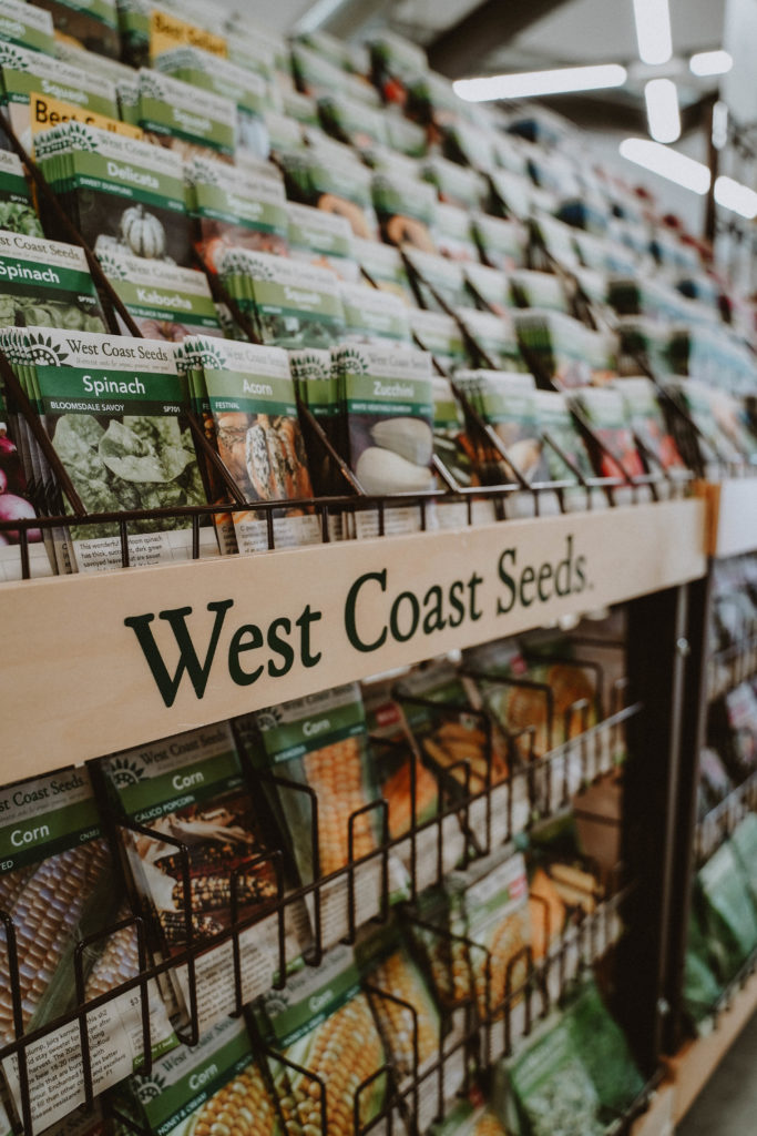 Many seed packets rest on a shelf that is labeled "West Coast Seeds"