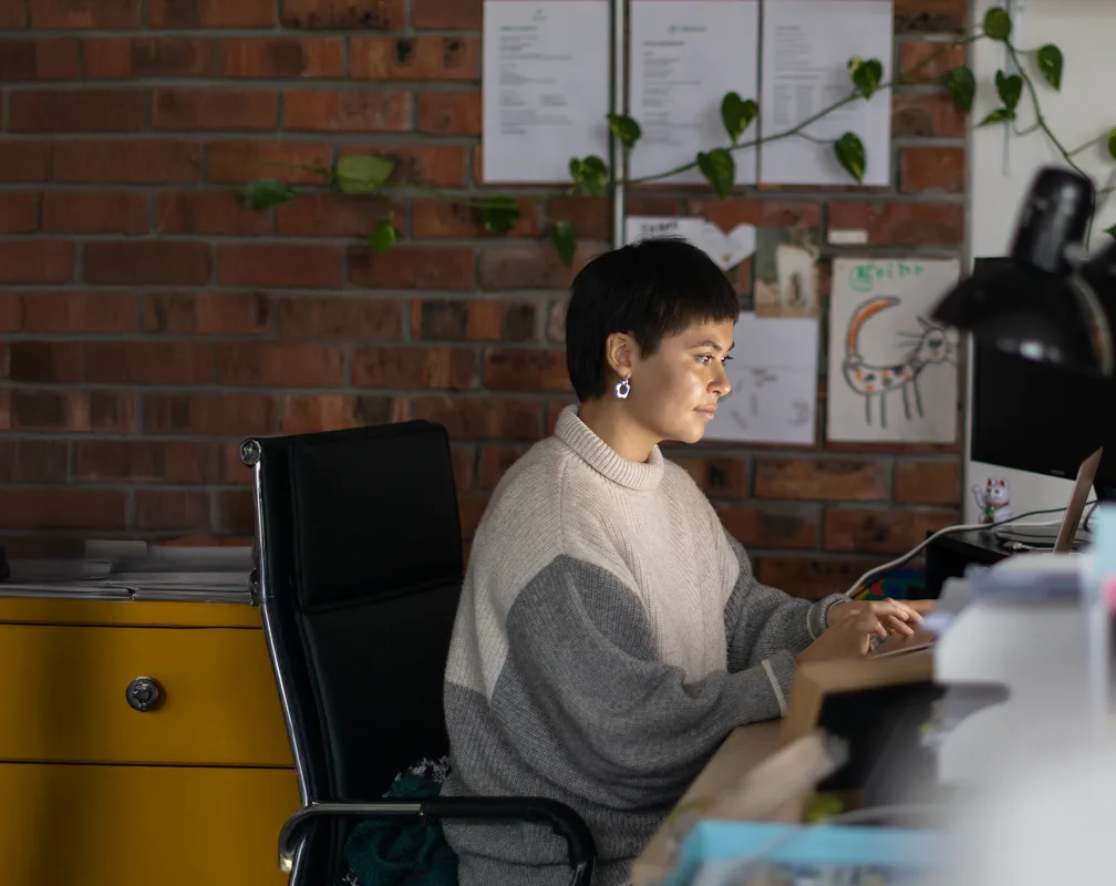 Person working at a desk in front of a brick wall with notes and plants