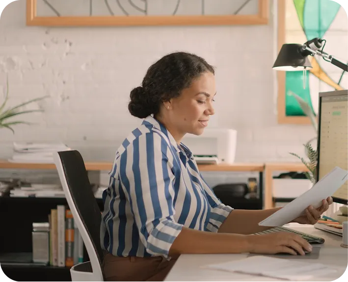 Woman reviewing an order sheet at her desk while working on a computer