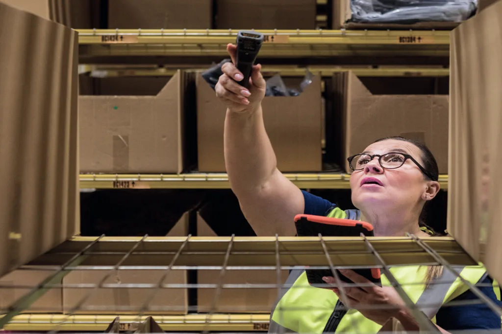 Warehouse worker reaching for a shelf bin while holding a handheld scanner